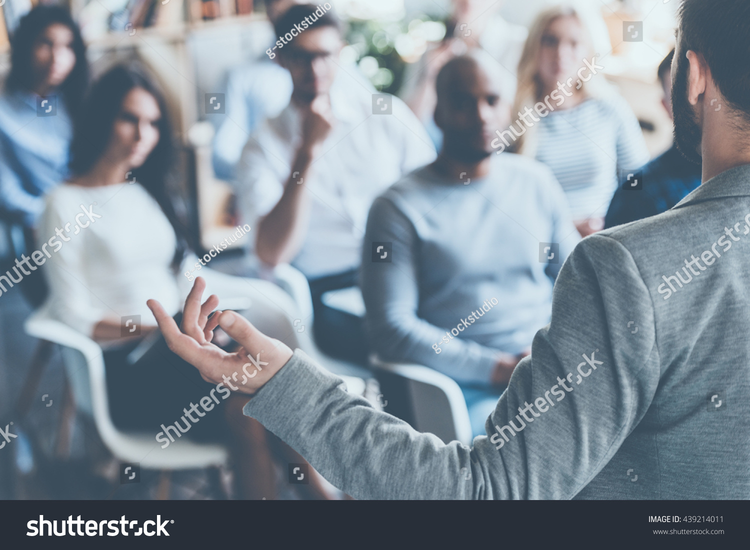 stock-photo-business-coach-rear-view-of-man-gesturing-with-hand-while-standing-against-defocused-group-of-439214011